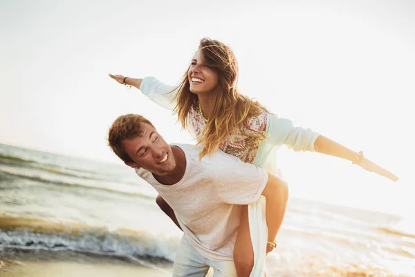Knappe jonge man geeft piggyback Ride naar vriendin op het strand. — Stockfoto