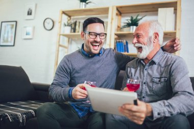 Portrait of senior man with adult son using digital tablet at ho
