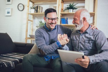 Portrait of senior man with adult son using digital tablet at ho