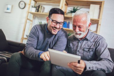 Portrait of senior man with adult son using digital tablet at ho
