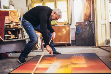 Sanat stüdyosunda tuvale resim yapan olgun bir adam..