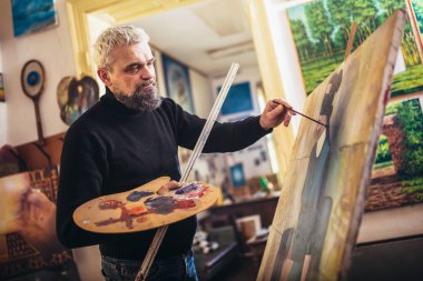 Sanat stüdyosunda tuvale resim yapan olgun bir adam..