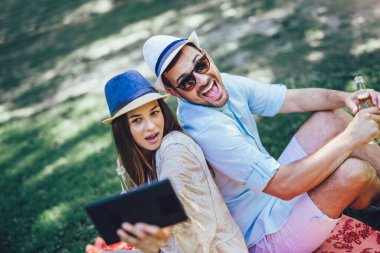 İki meyvelerle dolu bir piknik sepeti ile bir parkta piknik battaniye yatan, onlar dijital tablet kullanıyorsanız