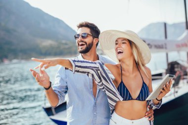 Mutlu genç çift turistik bir deniz beldesidijital tablet kullanarak liman tarafından yürüyüş