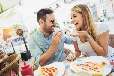 Couple eating pizza outdoors and smiling.They are sharing pizza in a outdoor cafe. clipart