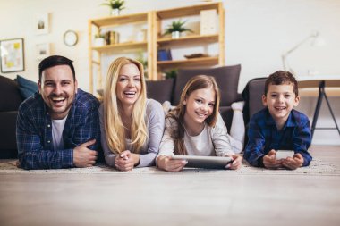 Dört kişilik genç bir aile hafta sonları oturma odasında dinleniyor ve dijital tablette film ya da çizgi film izliyor.
