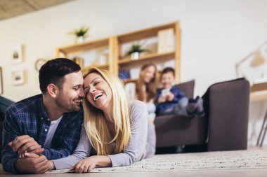 Birlikte vakit geçirin. Dört kişilik mutlu bir aile evde eğleniyor, çocuklar telefonla oynuyor, aileler yerde, birbirlerine sarılıyorlar.