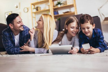 Dört kişilik genç bir aile hafta sonları oturma odasında dinleniyor ve dijital tablette film ya da çizgi film izliyor.