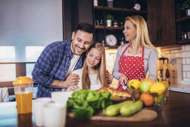 Kız ve güzel ailesi evde yemek pişirirken sebze kesip gülümsüyorlar.