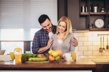 Güzel genç çift evde mutfakta sağlıklı yemekler pişirirken konuşuyor ve gülümsüyor..