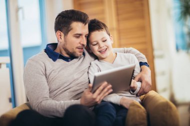 Baba ve oğul evde, bir tablet üzerinde oynarken eğleniyor