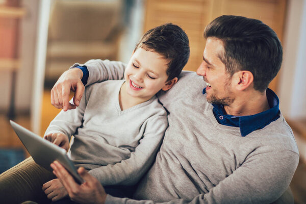 Father and son playing on a tablet at home, having fun