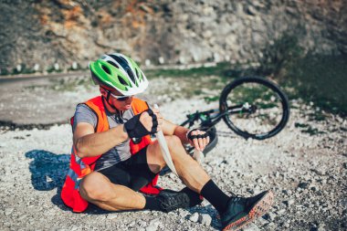 Bisikletçinin ilk yardım kiti bir bandaj kullanarak, kendine yardım etmek için bir bisikletten düştü. Bisiklet kazası. 