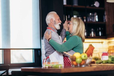 Güzel son sınıf çifti mutfakta birlikte yemek yaparken dans ediyor ve gülümsüyor. Karantinaya alın. Sağlık kavramı.