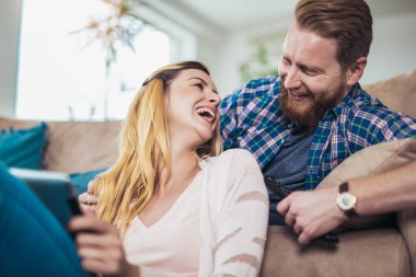 Birbirini seven bir çift kanepede oturur ve dijital tablet kullanır, eğlenir.. 