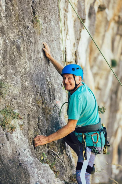 Senior man with a rope climbing on the rock.