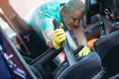 Adam arabanın içini elektrikli süpürgeyle temizliyor.