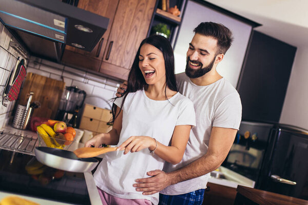Женщина готовит еду на плите с партнером позади нее на кухне