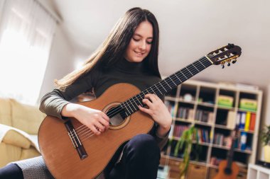 Güzel kız evdeki gitarda yeni bir ses alıştırması yapıyor.