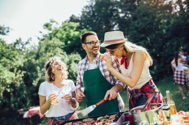 Bir grup insan mangal yapıyor, sohbet ediyor, içiyor ve yemek yiyor..