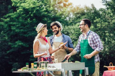 Bir grup insan mangal yapıyor, sohbet ediyor, içiyor ve yemek yiyor..
