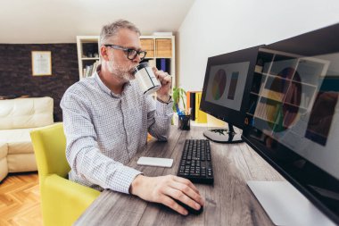 Evde bilgisayar kullanarak çalışan olgun bir adam..