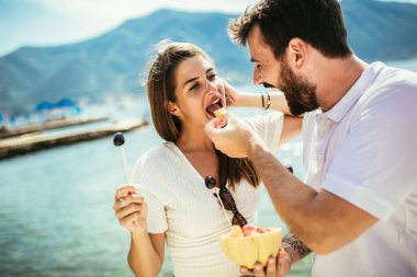 Arkadaşları ve sağlıklı gıda konsepti ile plajda meyve yiyen genç çift- yaz partisi
