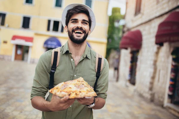 年轻人吃了一块开胃的披萨 饥饿的家伙手里拿着一块披萨 看着他 然后要吃了它 — 图库照片
