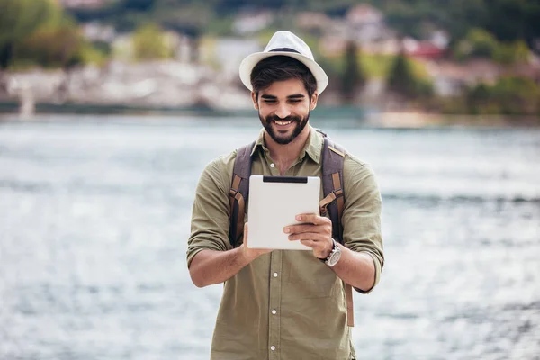 ボートを背景にした観光用の海のリゾートの港を歩く若い男 デジタルタブレットを保持 — ストック写真