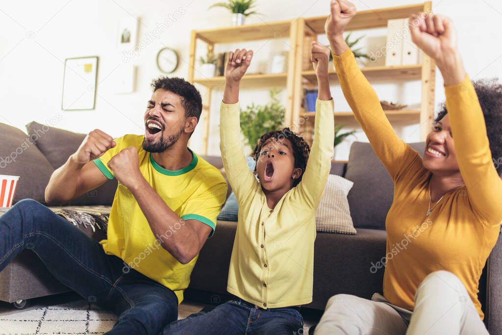 Happy African American family of three watching tv and cheering sport games on sofa at home