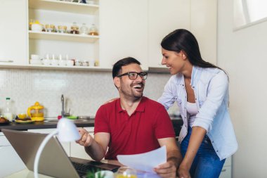 Genç çift finans işlerini yönetiyor, banka hesaplarını gözden geçiriyorlar modern mutfakta dizüstü bilgisayarlarını kullanıyorlar..