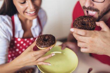 Neşeli genç çift mutfakta kahvaltı edip donut yiyor..