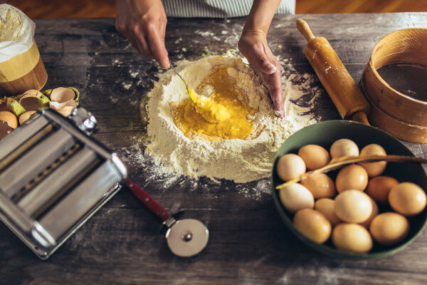 Hands whipping eggs into raw tough on wooden table.Ingredients for italian homemade pasta
