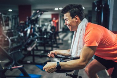 Spor salonunda bisiklete binen, bacak çalıştıran kardiyo antrenmanı yapan bisiklet süren bir adam..