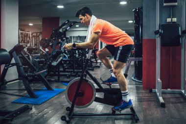 Spor salonunda bisiklete binen, bacak çalıştıran kardiyo antrenmanı yapan bisiklet süren bir adam..