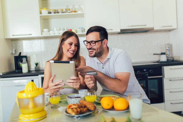 Couple spending money online on the internet, and having breakfast in the kitchen.