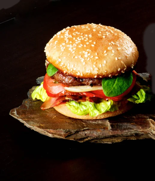 ベーコン レタス トマト バジル ローストした玉ねぎ ジューシーなソースの新鮮なおいしいハンバーガー暗い背景に石のボード上のセサミバンにクローズアップ — ストック写真