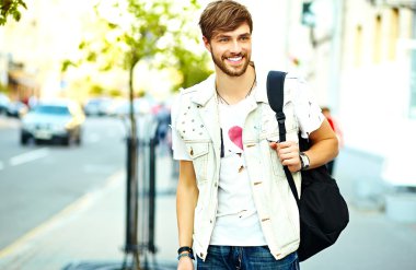 Funny smiling hipster handsome man in stylish summer clothes posing on street background 