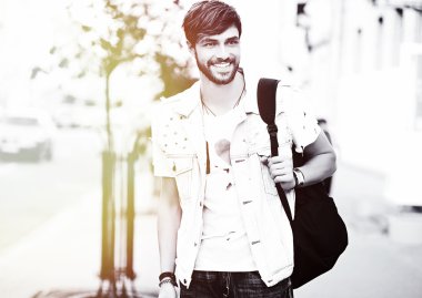 Funny smiling hipster handsome man in stylish summer clothes posing on street background 