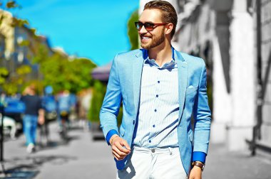 Yüksek moda bakmak. Takım elbise li genç şık, mutlu yakışıklı işadamı modeli güneş gözlüğü ile sokakta yürüyor