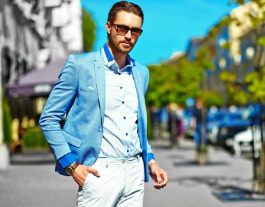 Yüksek moda bakmak. Takım elbise li genç şık, mutlu yakışıklı işadamı modeli güneş gözlüğü ile sokakta yürüyor