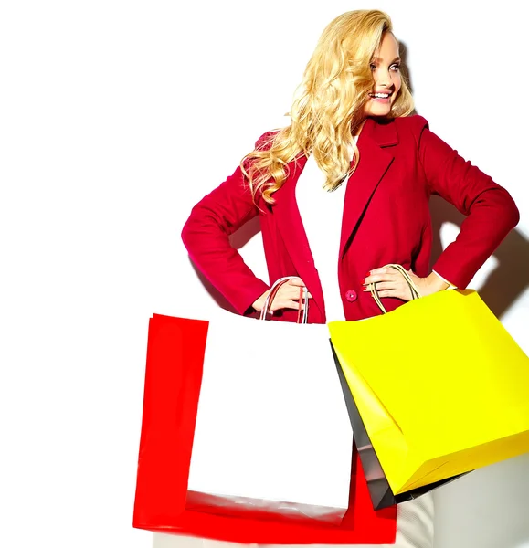 Portret van mooie schattige gelukkig zoete glimlachende blonde vrouw meisje houden in haar handen groot winkelen kleurrijke tassen in rode jas hipster geïsoleerd op wit — Stockfoto
