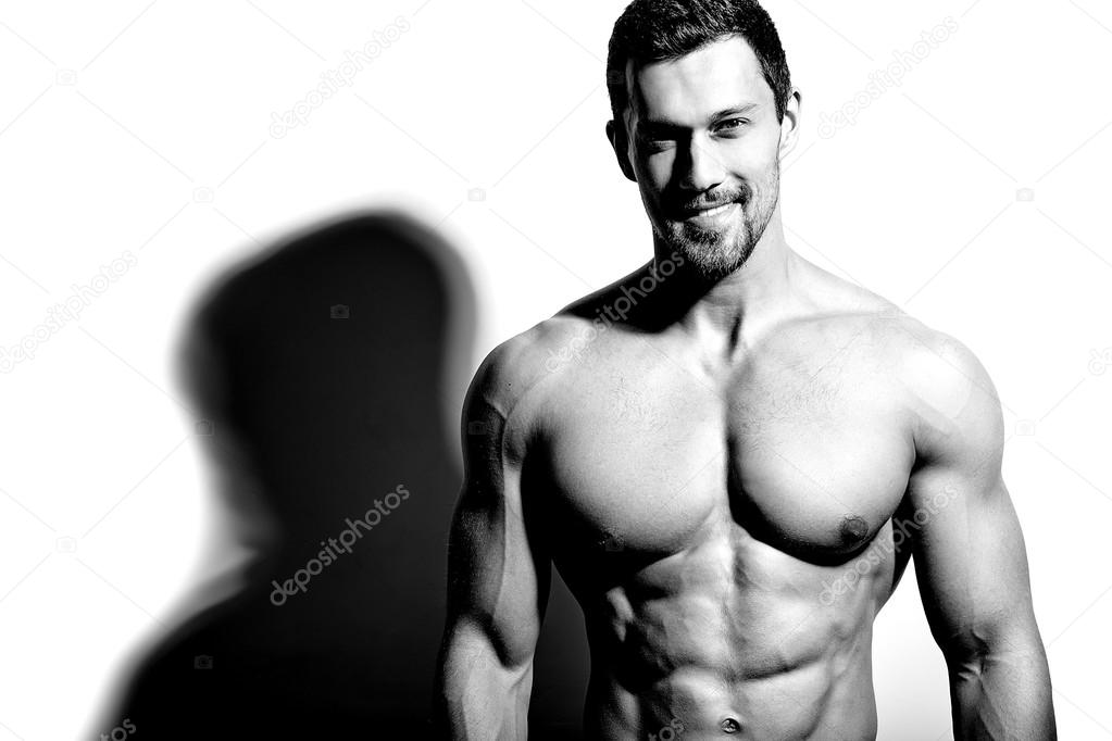 Portrait of strong healthy handsome Athletic Man Fitness Model posing near white wall