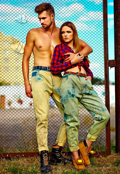 Sexy elegante loira jovem modelo com maquiagem brilhante com pele bronzeada perfeita e homem musculado bonito em jeans ao ar livre — Fotografia de Stock