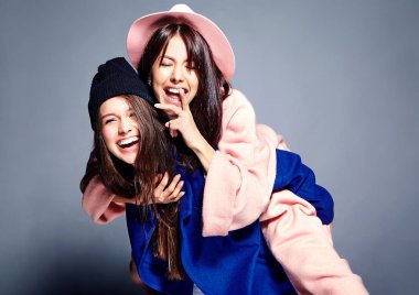 iki esmer bayan modelleri yaz casual hipster palto gri arka plan üzerinde poz içinde gülümseyen moda portre. Birbirlerine arkasında tutarak kızlar 