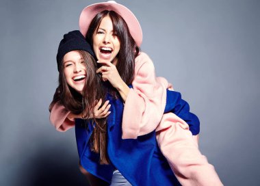 iki esmer bayan modelleri yaz casual hipster palto gri arka plan üzerinde poz içinde gülümseyen moda portre. Birbirlerine arkasında tutarak kızlar 