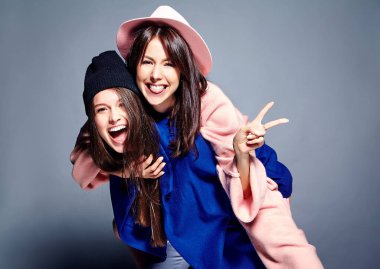 iki esmer bayan modelleri yaz casual hipster palto gri arka plan üzerinde poz içinde gülümseyen moda portre. Birbirlerine arkasında tutarak kızlar 