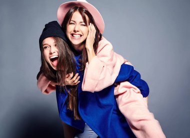 iki esmer bayan modelleri yaz casual hipster palto gri arka plan üzerinde poz içinde gülümseyen moda portre. Birbirlerine arkasında tutarak kızlar 