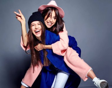iki esmer bayan modelleri yaz casual hipster palto gri arka plan üzerinde poz içinde gülümseyen moda portre. Birbirlerine arkasında tutarak kızlar 