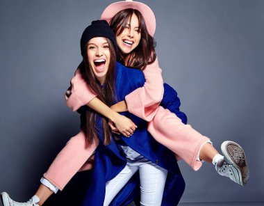 iki esmer bayan modelleri yaz casual hipster palto gri arka plan üzerinde poz içinde gülümseyen moda portre. Birbirlerine arkasında tutarak kızlar 